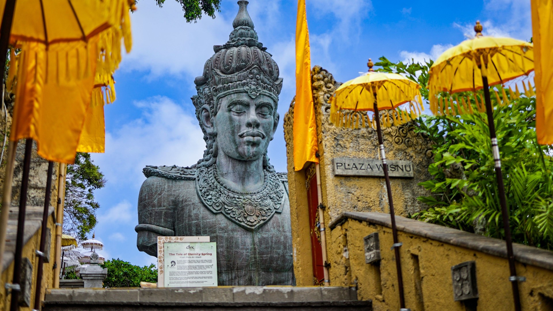 Vishnu statue at Plaza Vishnu surrounded by traditional yellow umbrellas at Garuda Wisnu Kencana Cultural Park, Bali, Indonesia